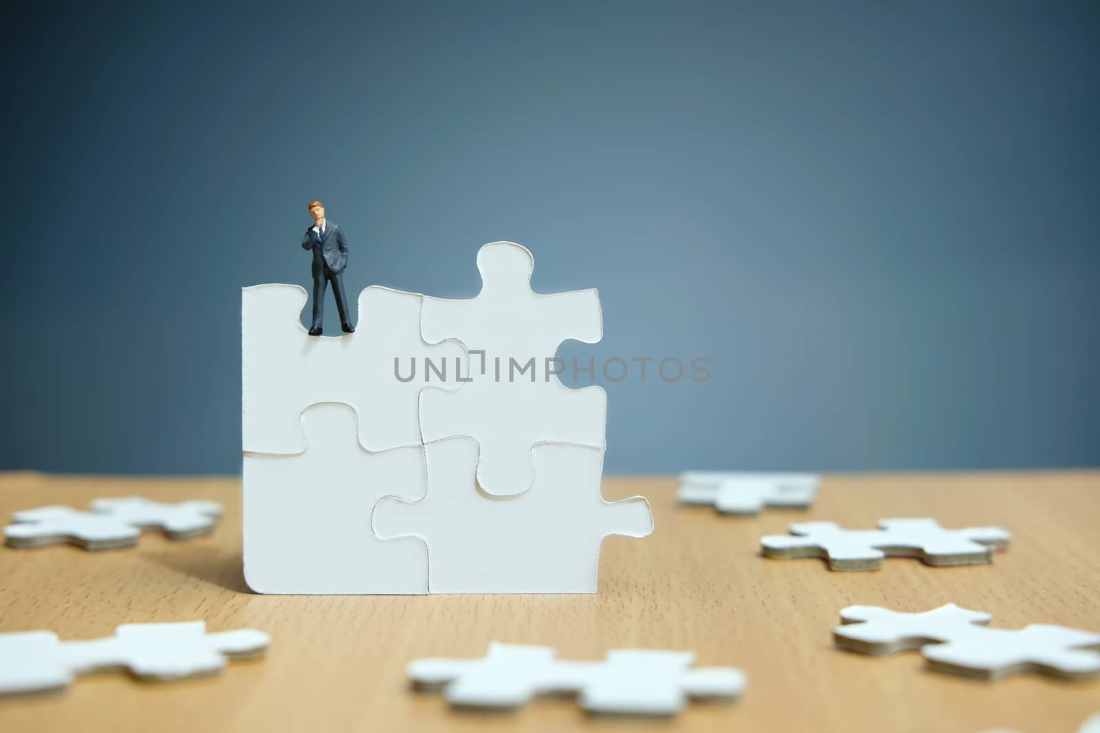 Conceptual photo of business strategy – miniature people standing on four joined jigsaw puzzle