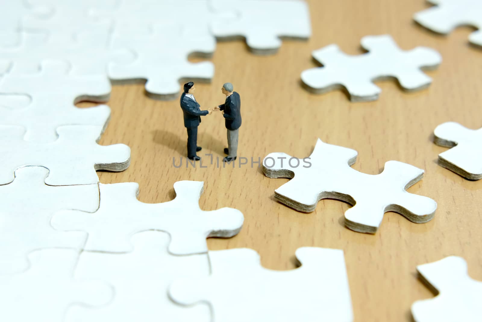 Business strategy conceptual photo - Miniature businessman make handshake partnership in the center of jigsaw puzzle piece