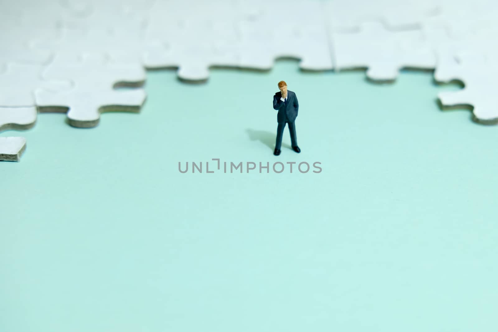 Business strategy conceptual photo - Miniature businessman thinking in front of puzzle jigsaw