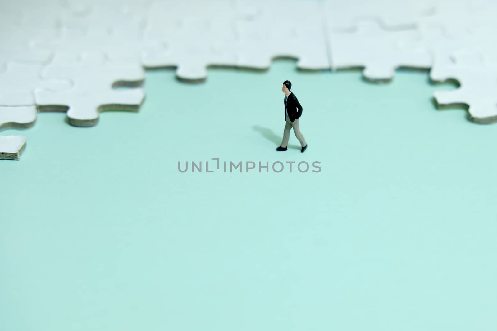 Business strategy conceptual photo - Miniature businessman walking in front of puzzle jigsaw