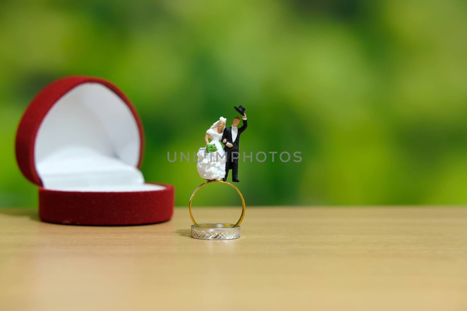 Miniature wedding concept. Bride and groom make greeting from above golden ring with dreamy green background