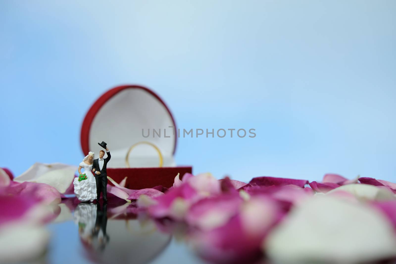 Miniature photography outdoor marriage wedding concept, bride and groom walking in front of opened ring box on red white rose flower pile by Macrostud