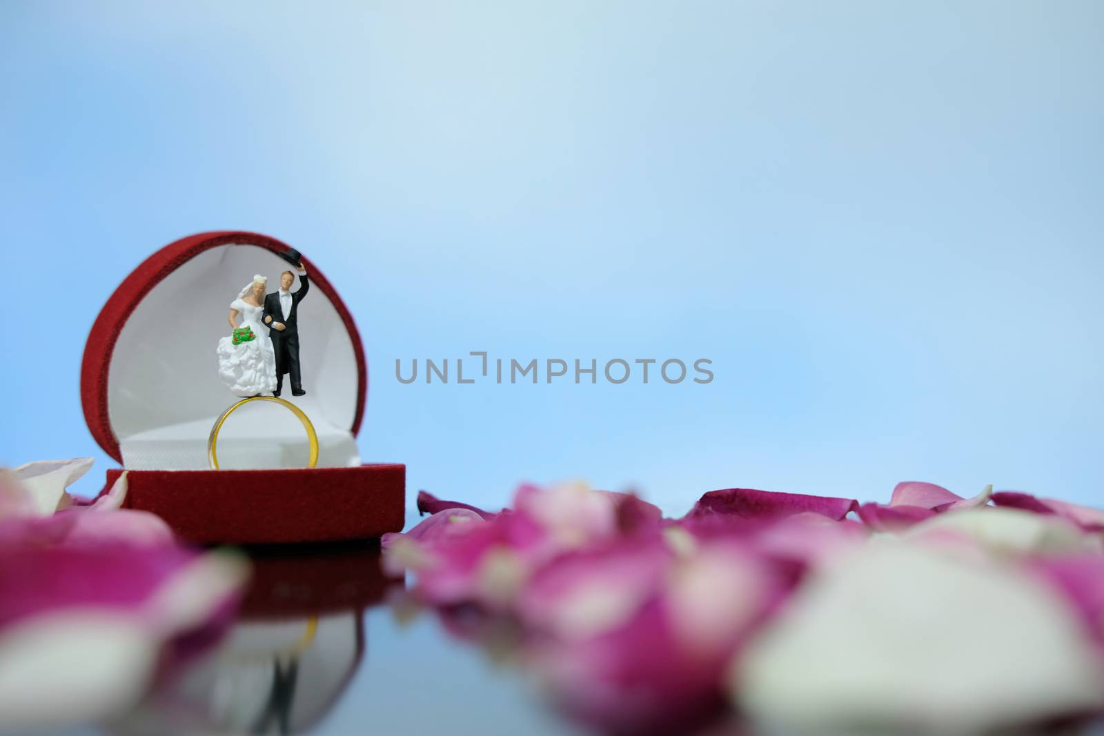 Miniature photography outdoor marriage wedding concept, bride and groom standing above opened ring box on red white rose flower pile by Macrostud