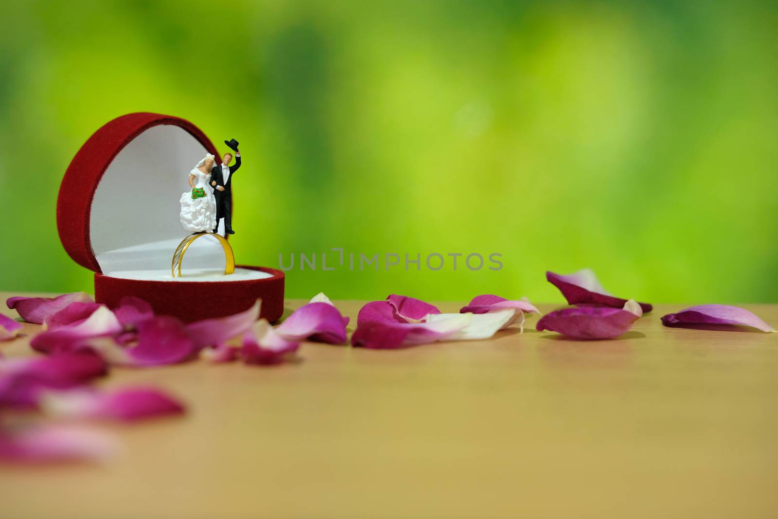 Miniature photography - outdoor garden wedding ceremony concept, bride and groom stand above ring box in the middle of red rose flower pile
