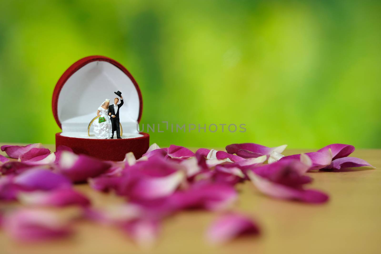 Miniature photography - outdoor garden wedding ceremony concept, bride and groom stand above ring box in the middle of red rose flower pile by Macrostud