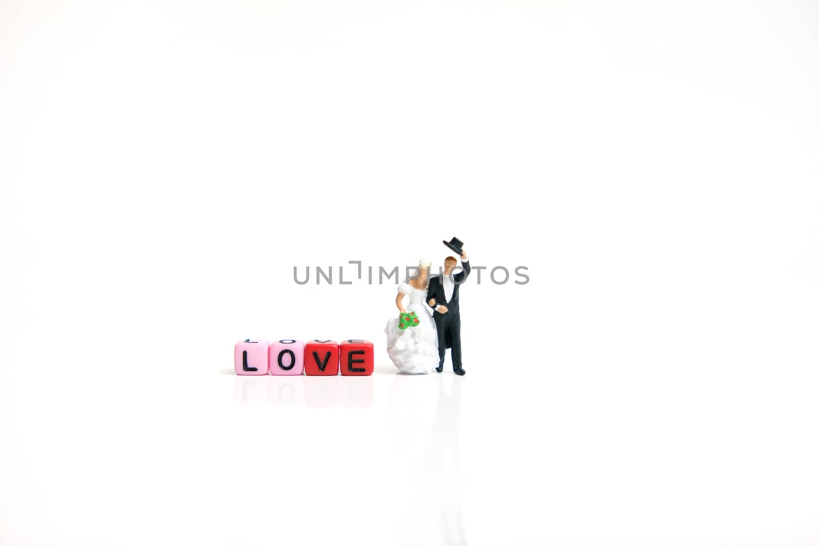 Miniature people photography. Bride and groom with love word beads on shiny white background by Macrostud