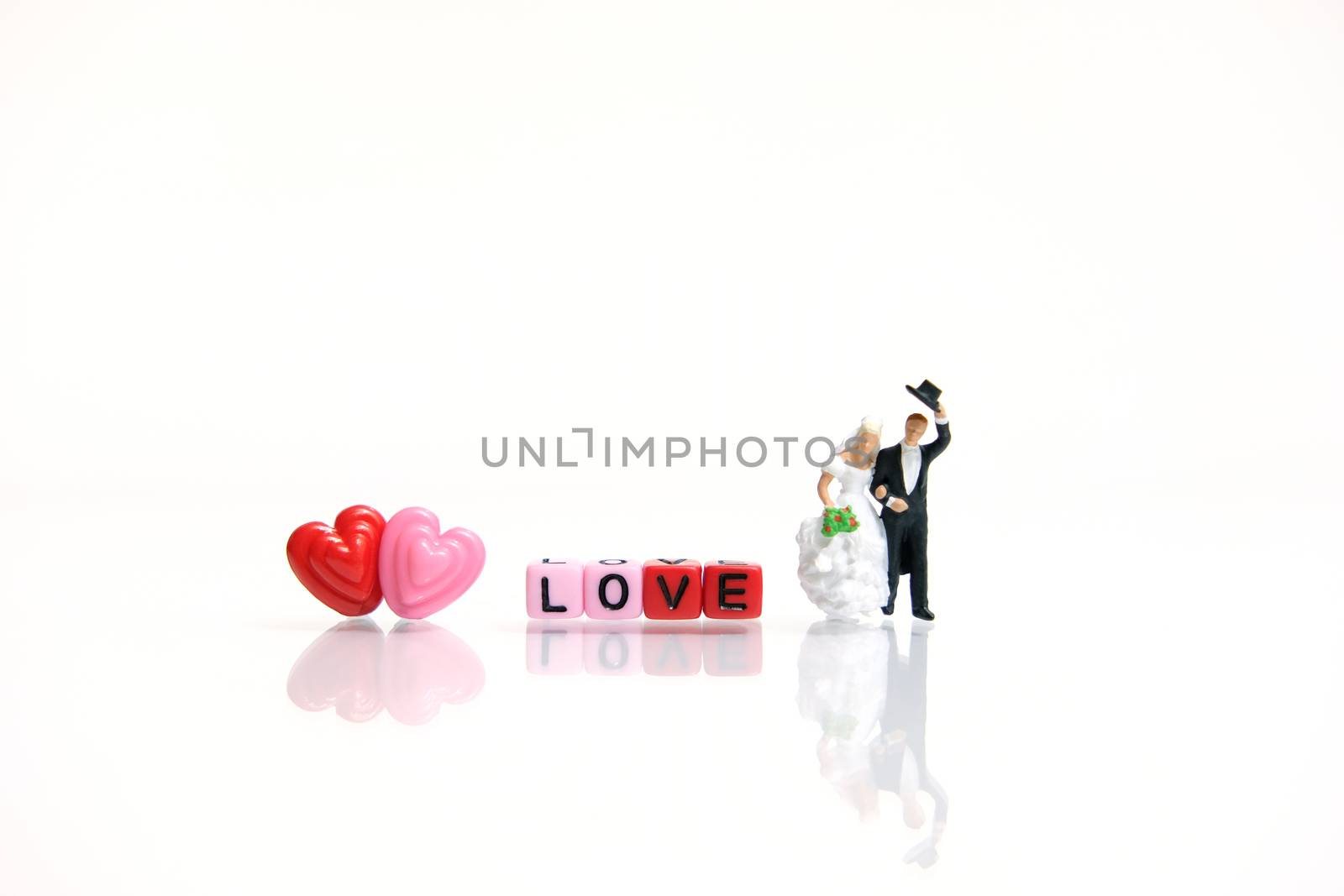 Miniature people photography for valentines day, bride and groom with heart shape and love word beads on shiny white background by Macrostud