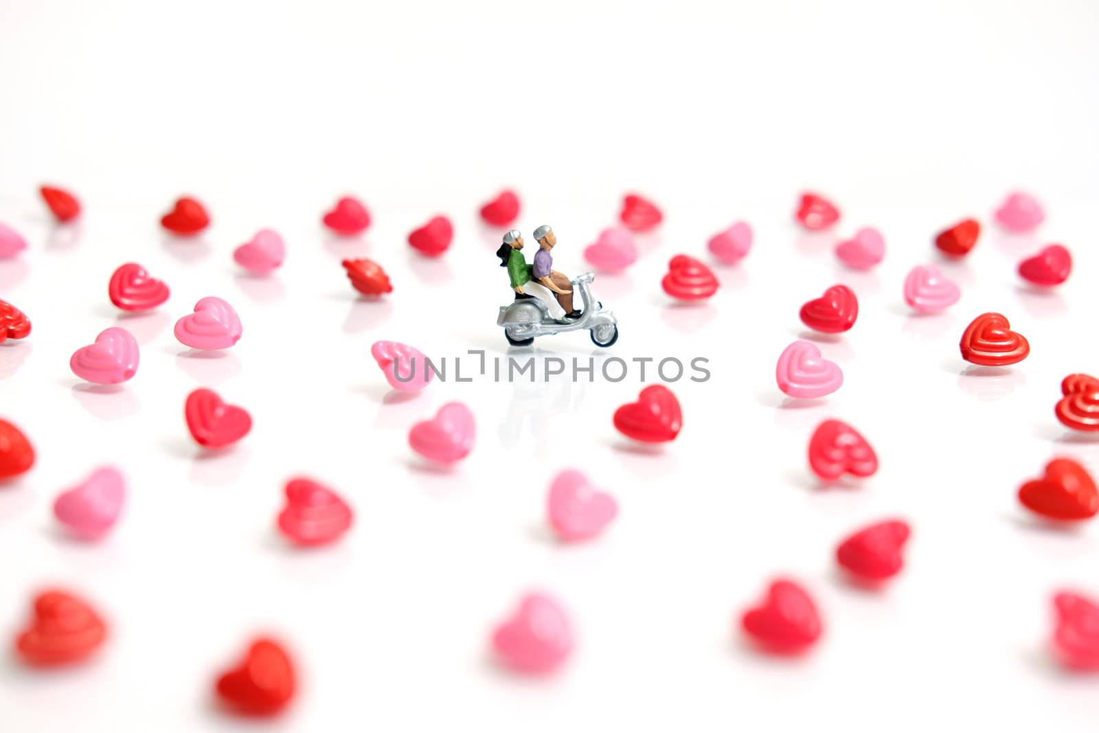 Miniature people photography for valentines day, young couple riding scooter with I love you beads on shiny white background by Macrostud