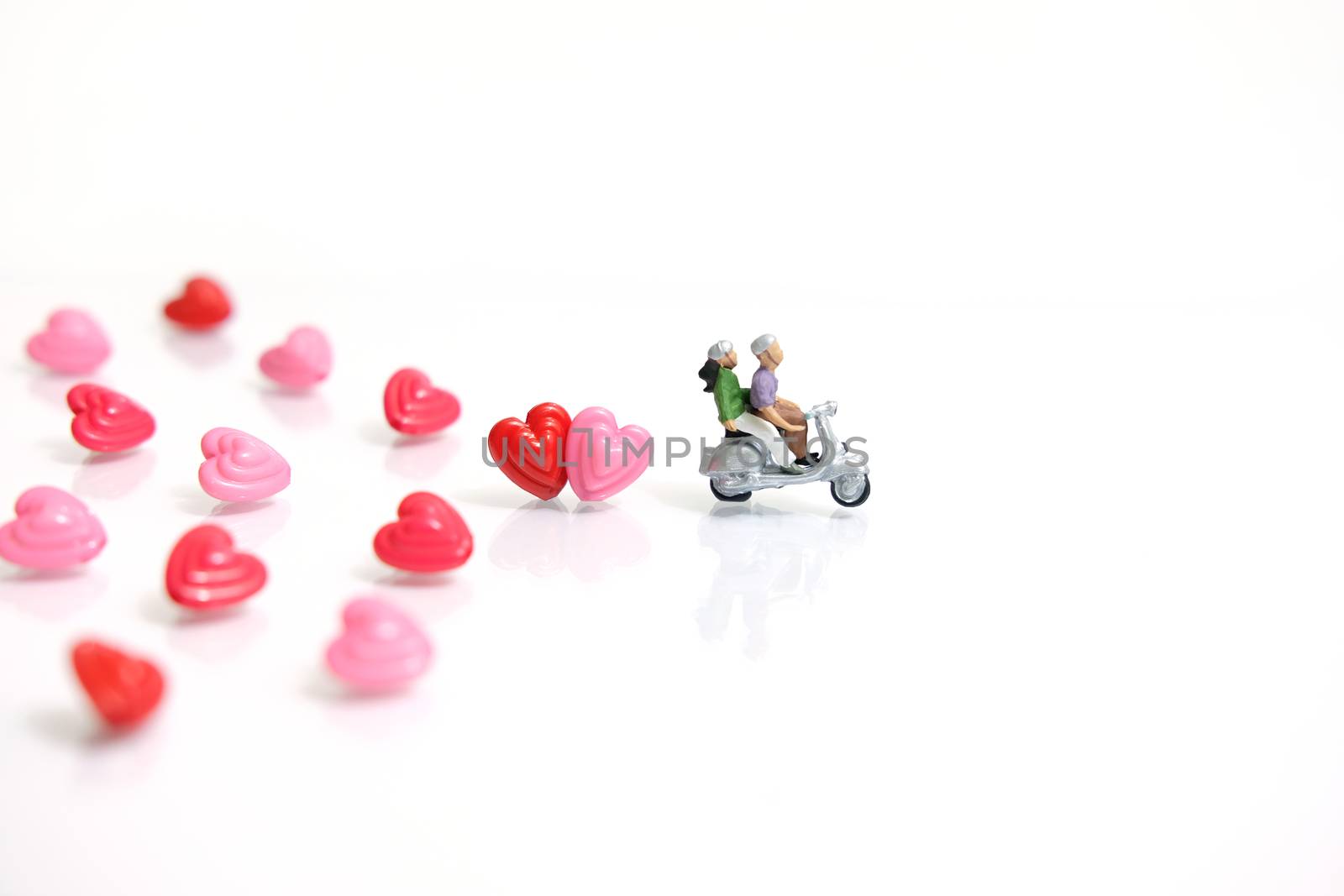 Miniature people photography for valentines day, young couple riding scooter with I love you beads on shiny white background