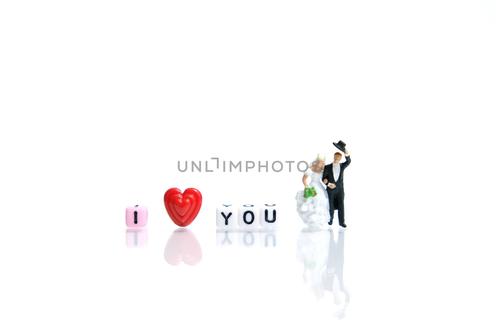 Miniature people photography for valentines day, bride and groom with heart shape and I love you word beads on shiny white background