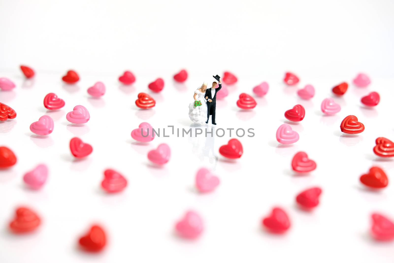 Miniature people photography. Bride and groom with heart shape and love word beads on shiny white background