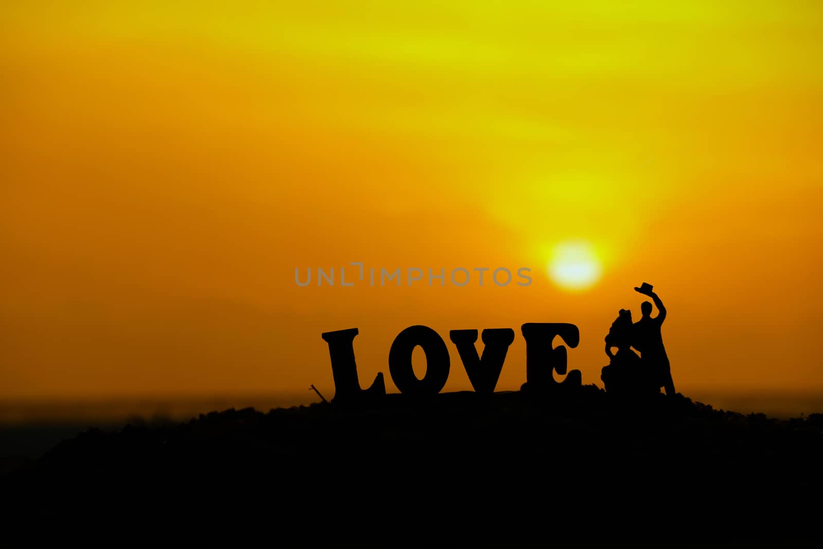 miniature people / toy photography - conceptual valentine holiday illustration. Bride and groom silhouette standing at the sand beach with love word block