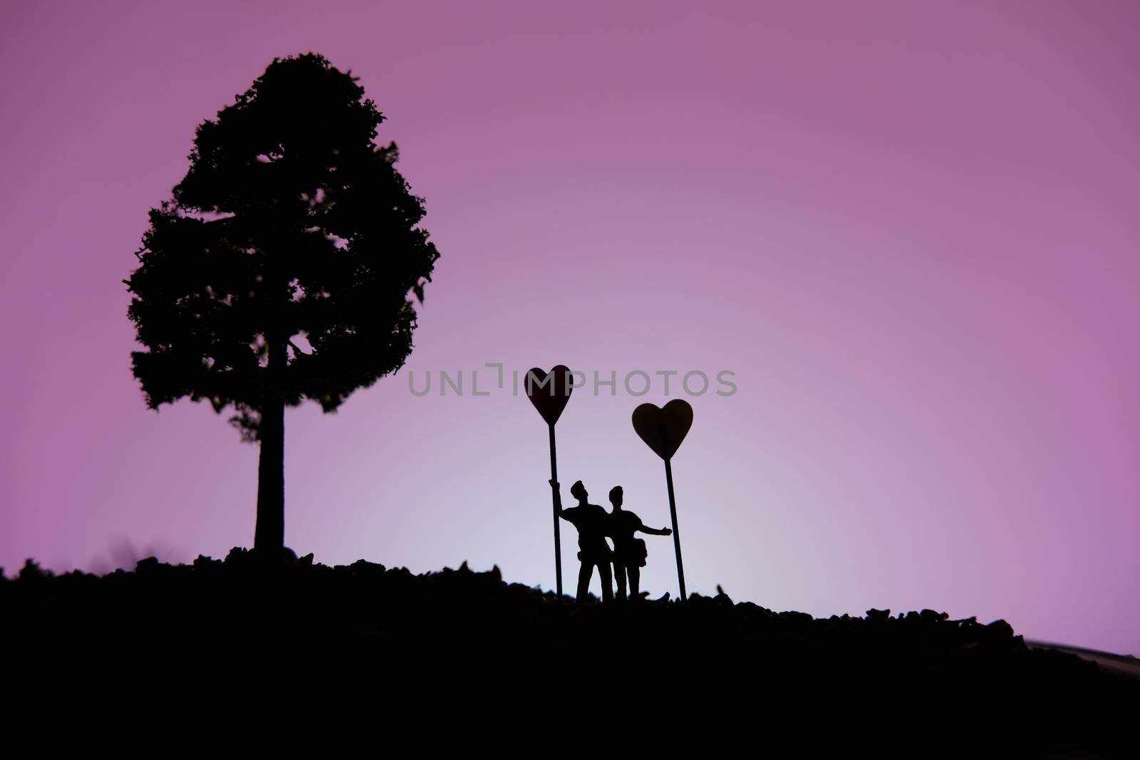 miniature people / toy photography - conceptual valentine holiday illustration. A Couple silhouette standing at the hill holding heart balloon