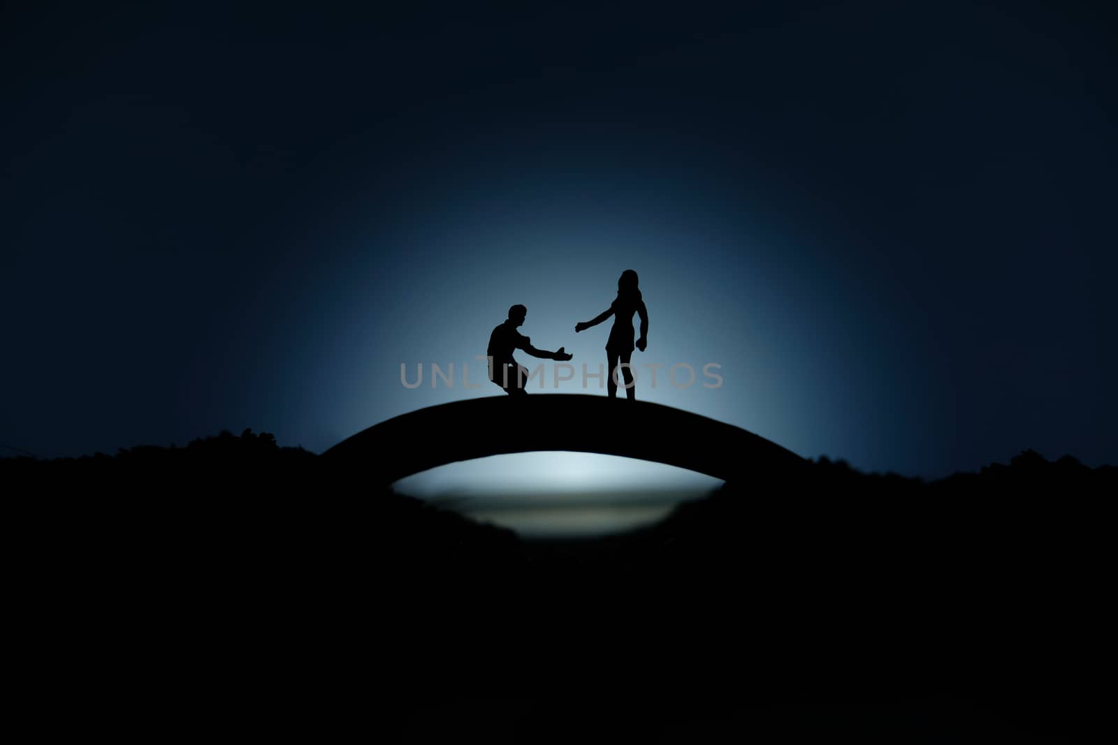 miniature people / toy photography - conceptual valentine holiday illustration. A man proposing a girl silhouette at the bridge under the moon light