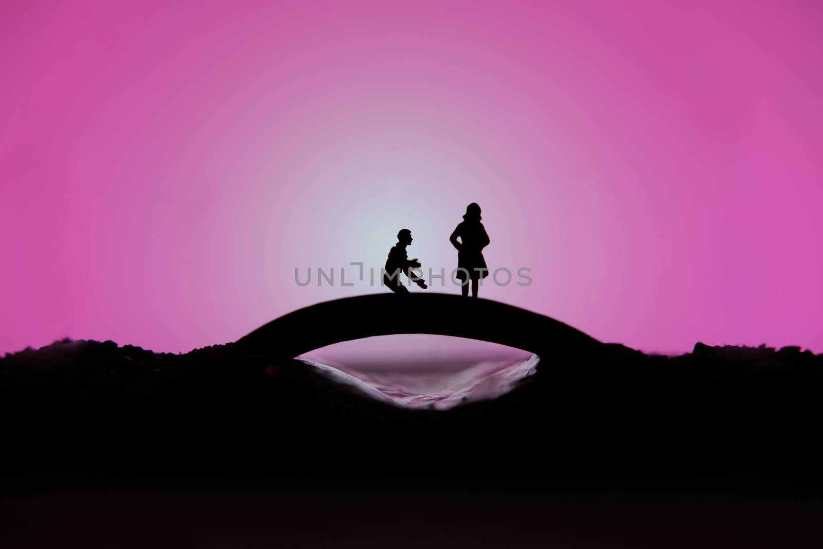 miniature people / toy photography - conceptual valentine holiday illustration. A man proposing a girl silhouette above the bridge