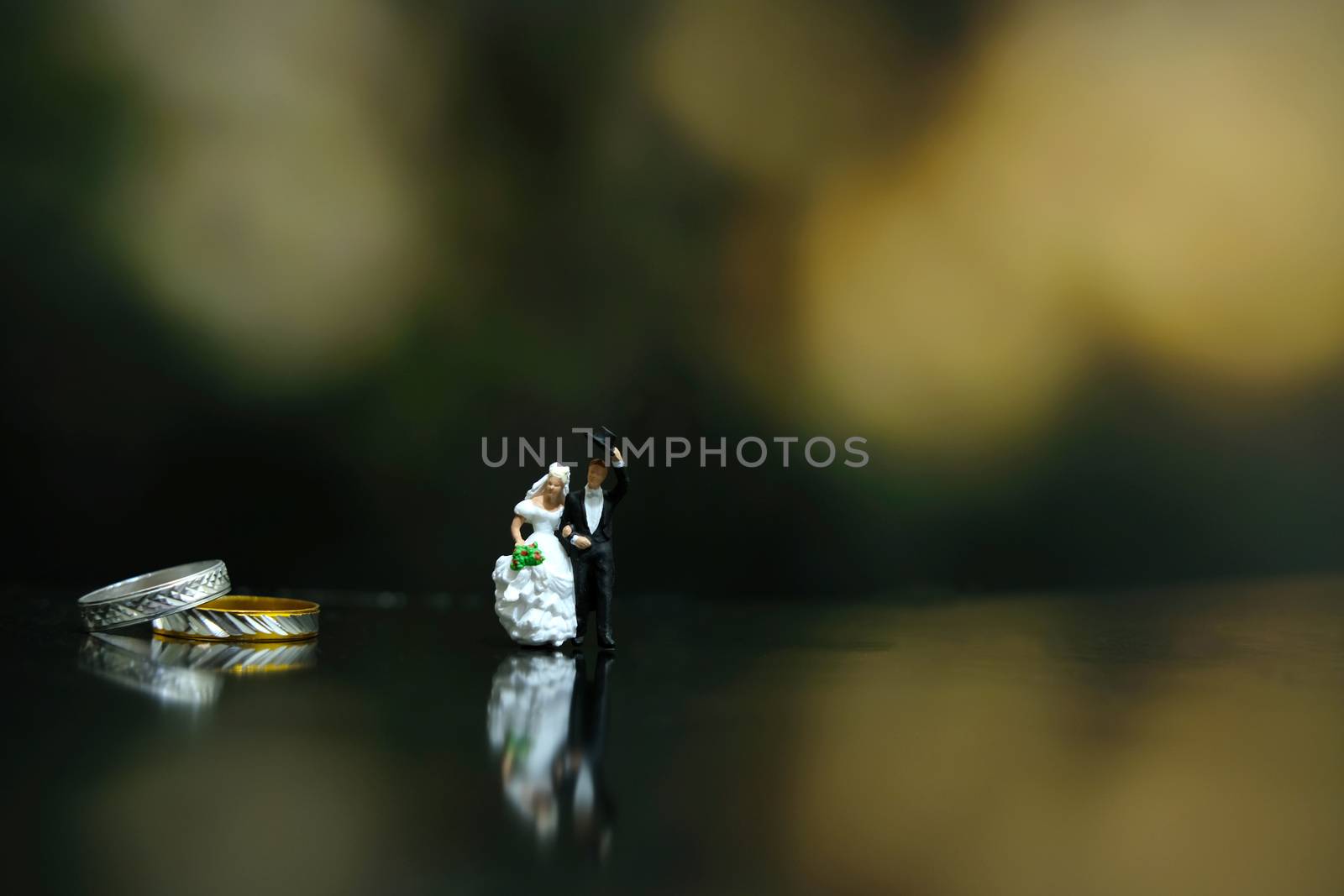 Miniature wedding concept - bride and groom walking on a shiny floor with couple ring
