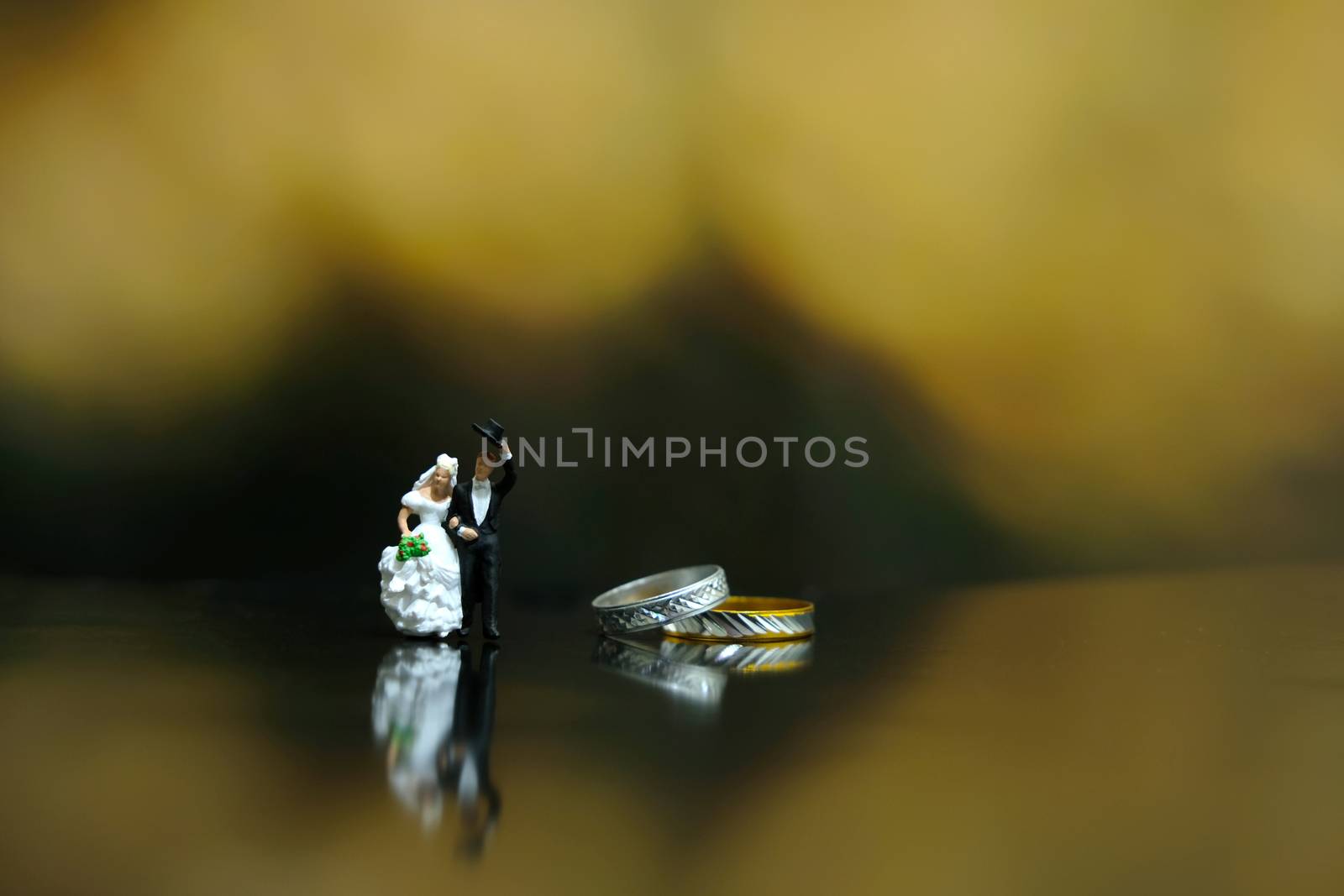 Miniature wedding concept - bride and groom walking on shiny floor beside their golden wedding ring