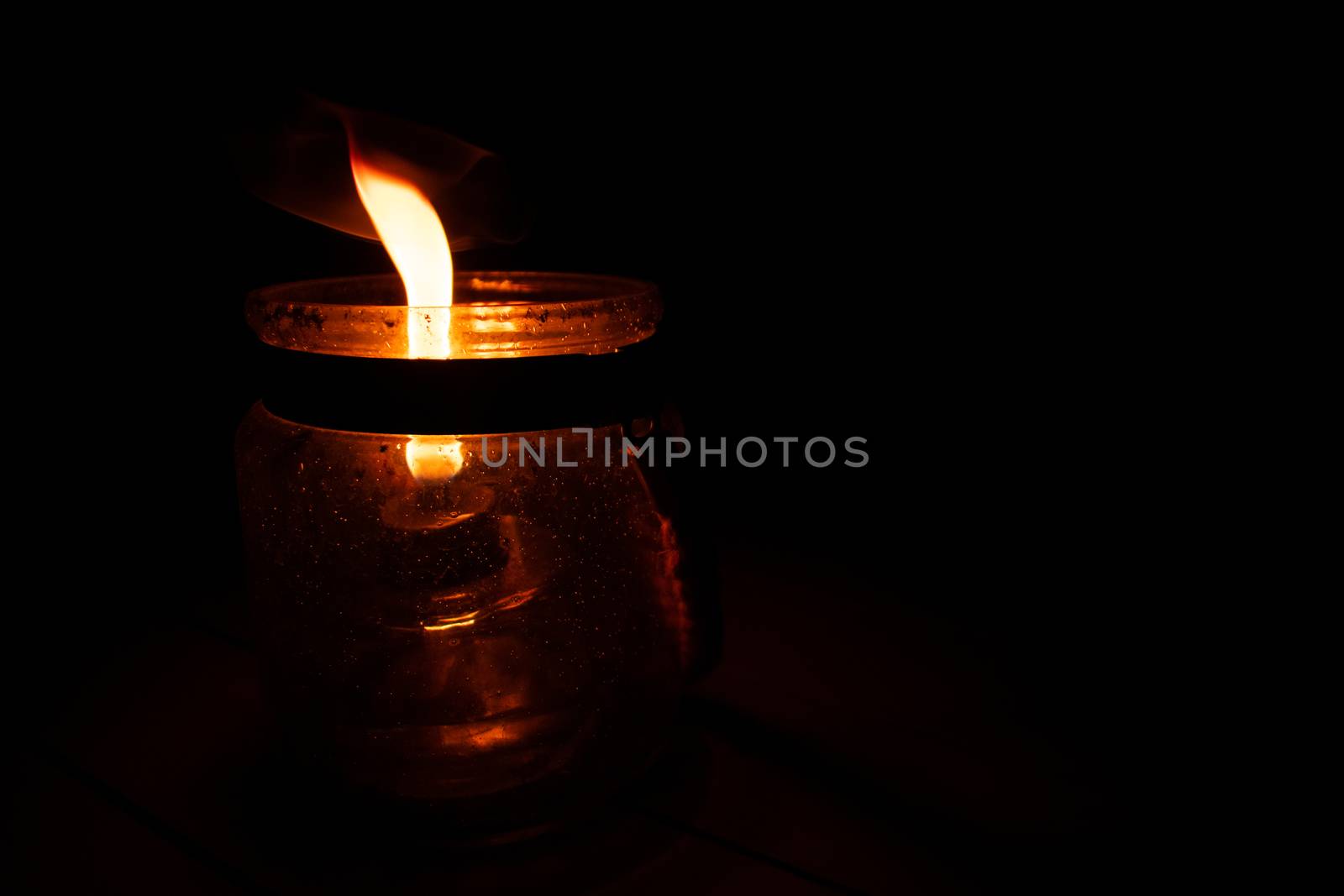 A Lit Candle Inside a Mason Jar on a Pure Darkness