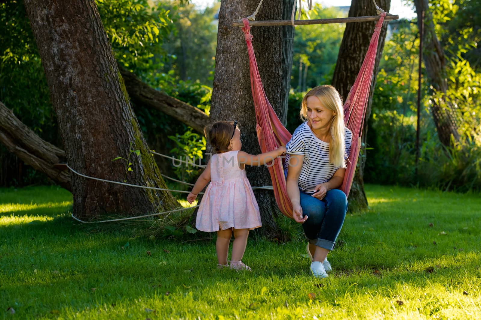 A young woman with a small child is sitting in a hammock in her garden.