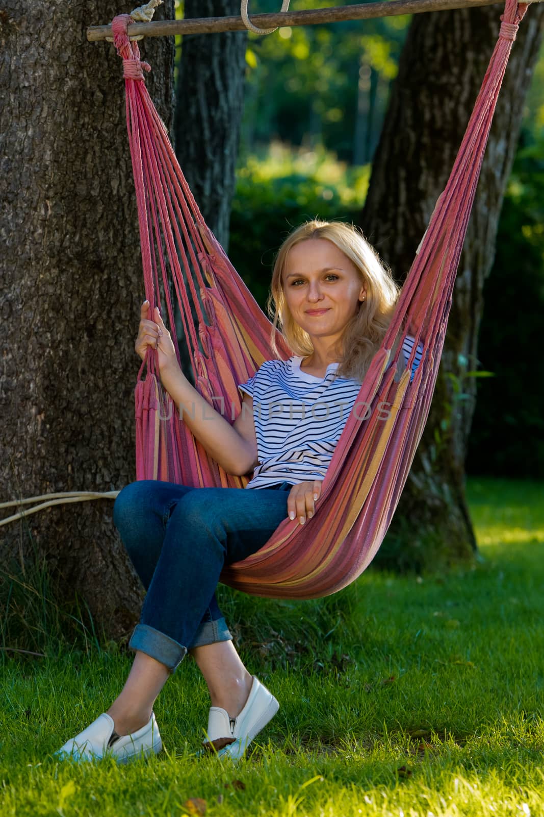 A young woman is sitting in a hammock in her garden.
