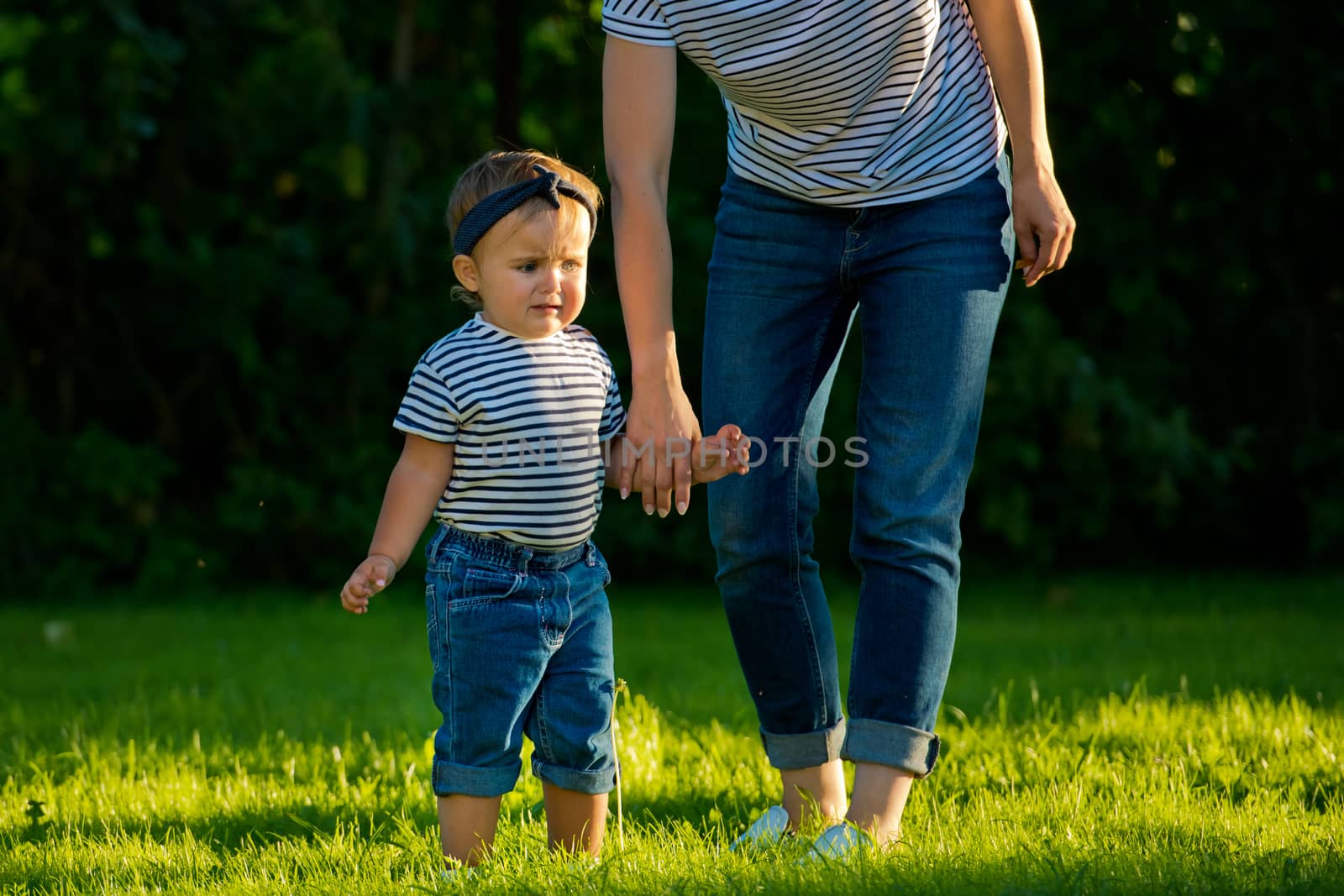 A young mother holds the hand of her little daughter on a green lawn in her garden.