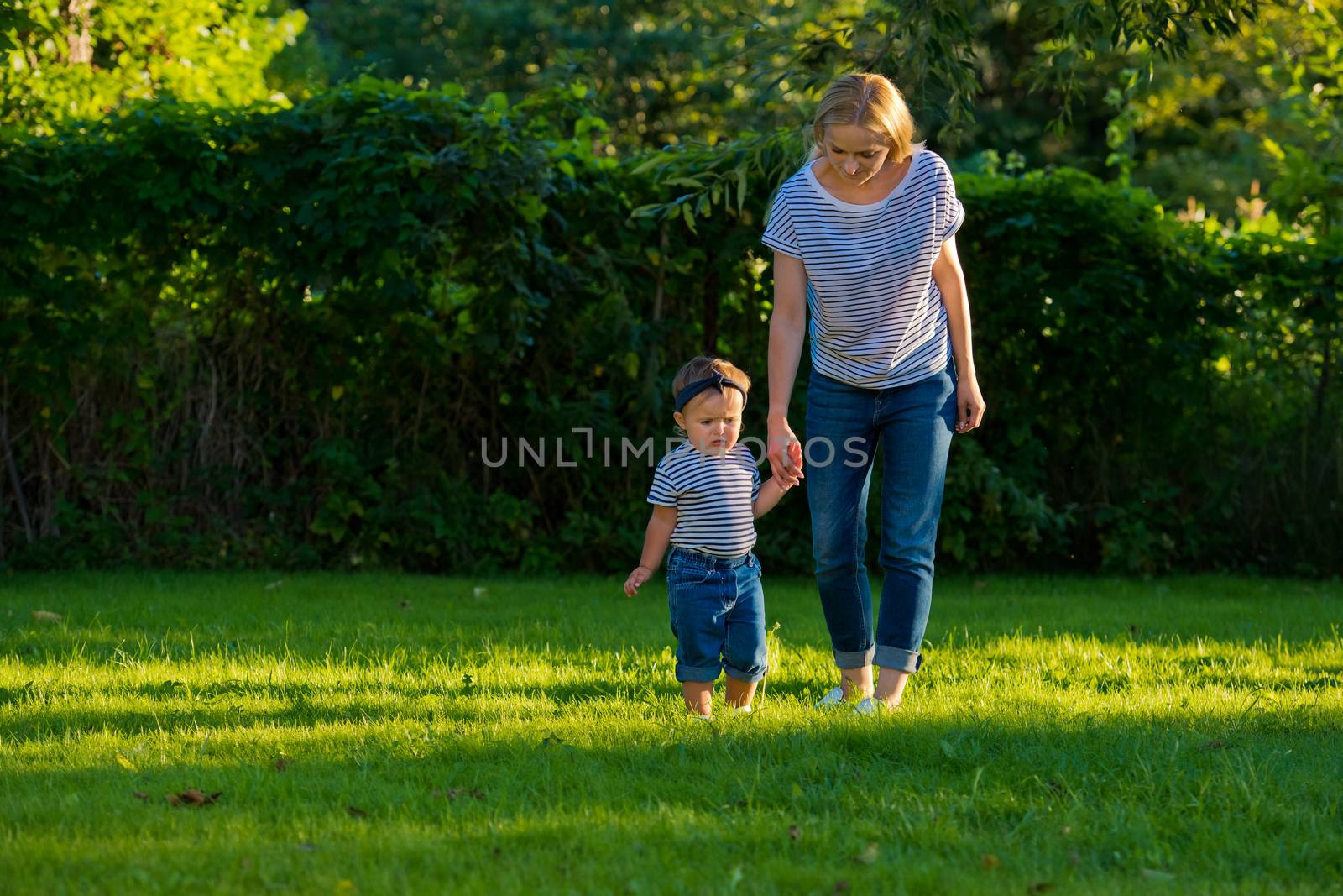 A young mother holds the hand of her little daughter on a green lawn in her garden.