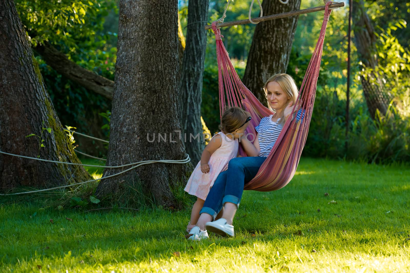 A young woman with a small child is sitting in a hammock in her garden.