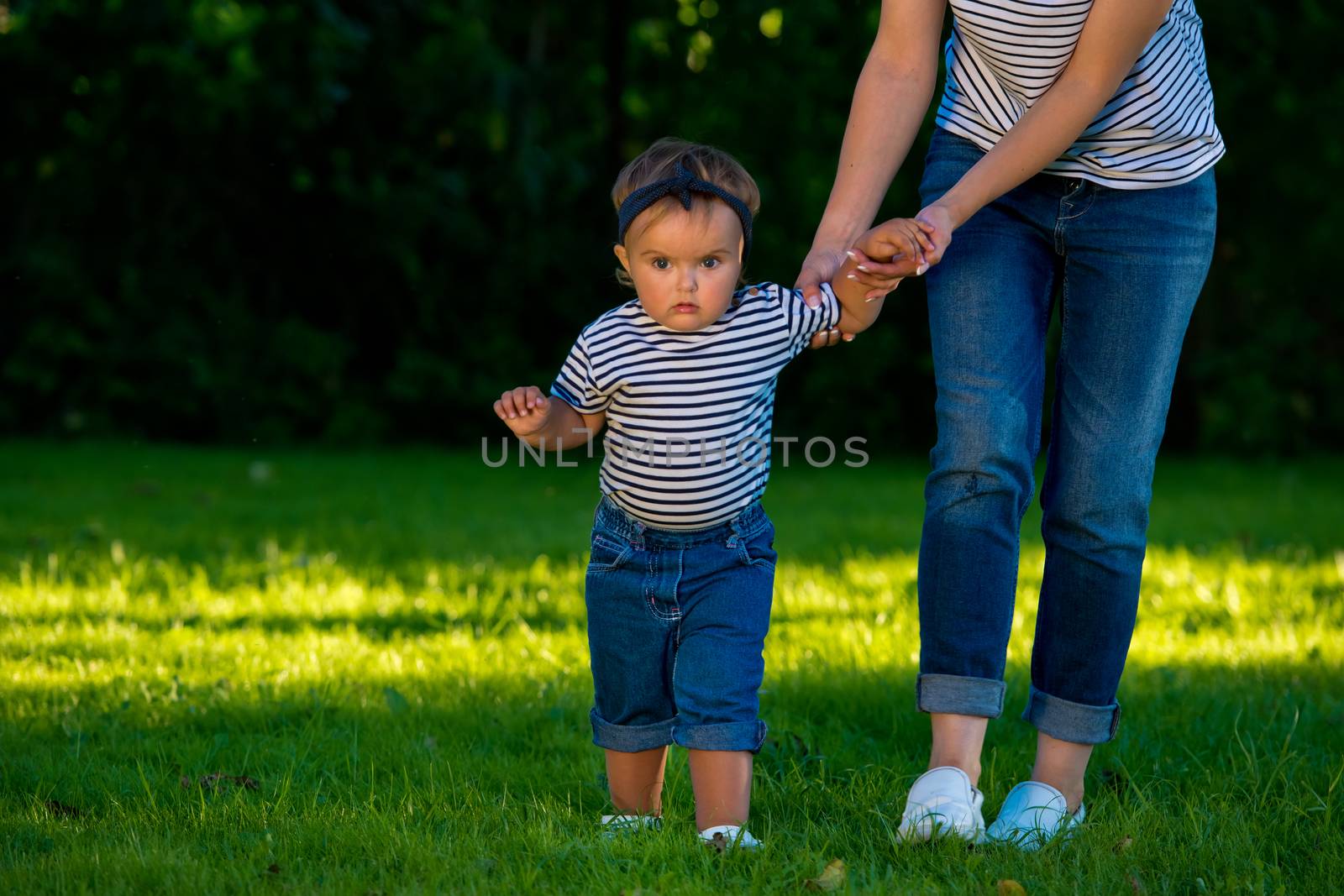 A young mother holds the hand of her little daughter on a green lawn in her garden.