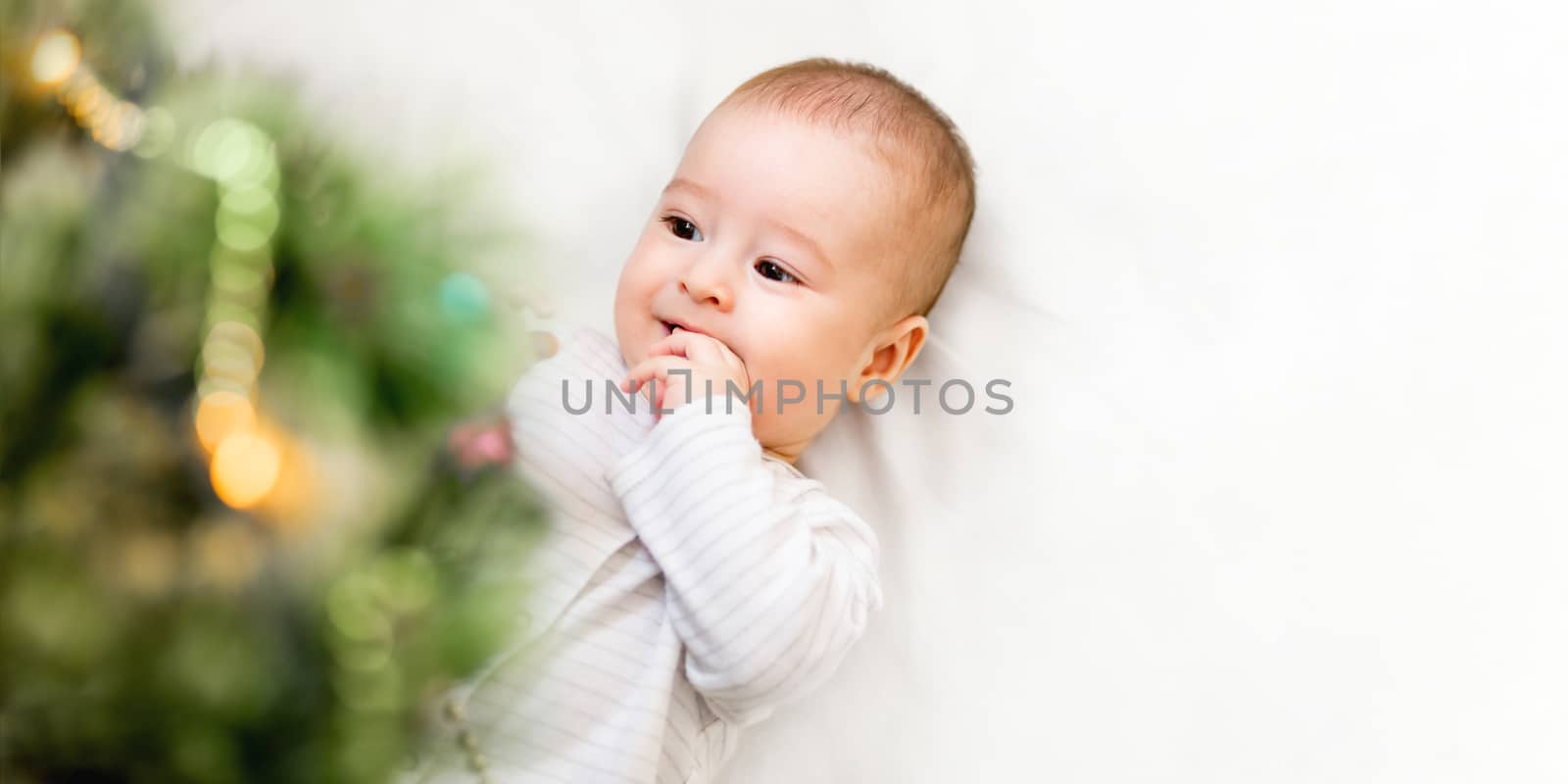 Baby boy or girl lying under Christmas tree. Little child plays by aksenovko