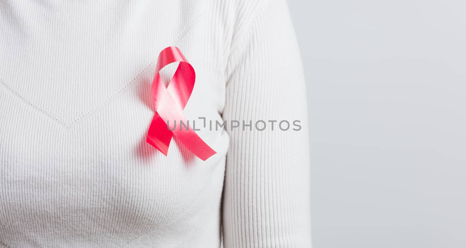 Breast cancer awareness healthcare and medicine concept. Close up Asian woman wear white shirt standing with pink breast cancer awareness ribbon pin on chest, studio shot isolated on white background