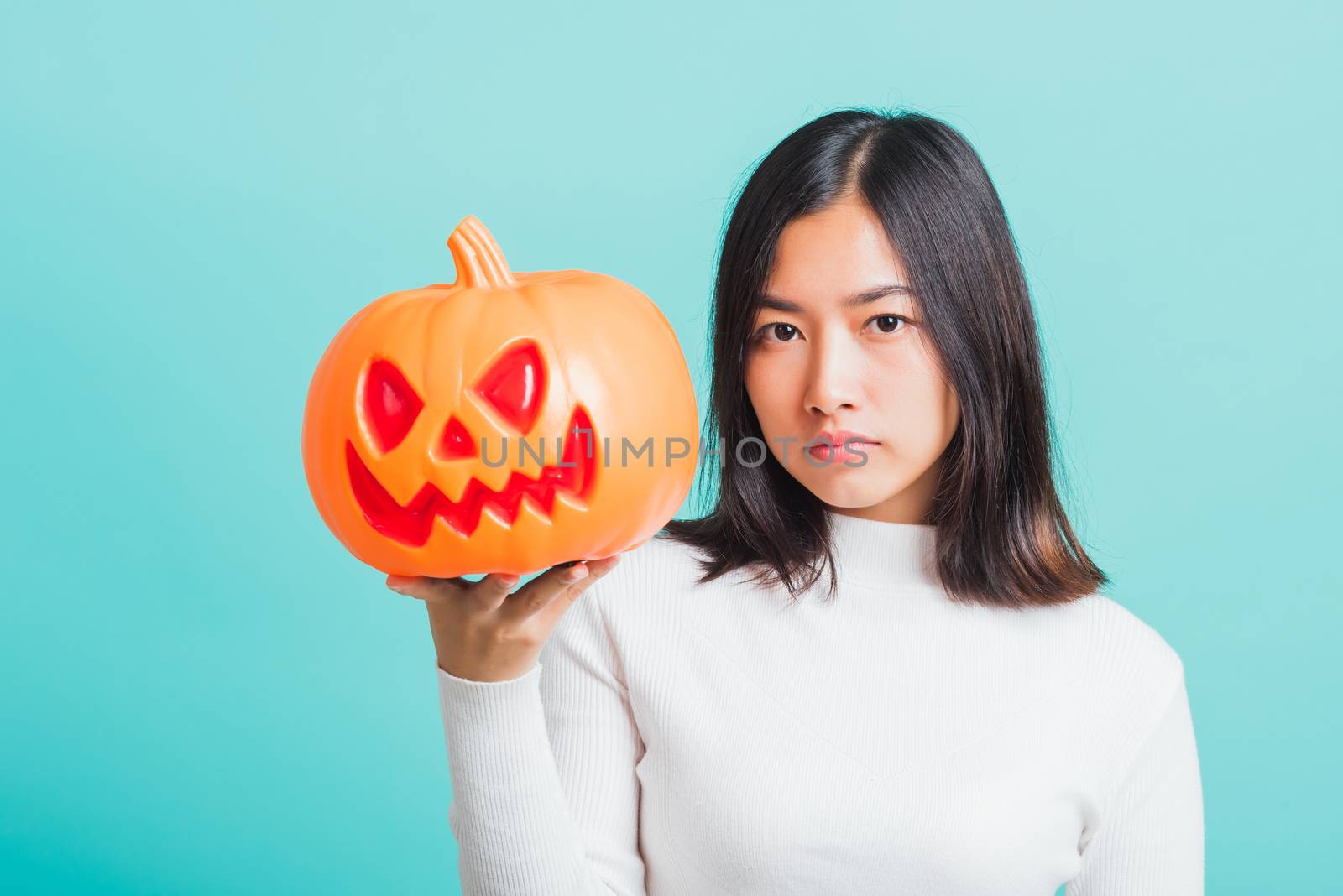 Portrait of Asian beautiful young woman holding orange model pumpkins, funny happy female with ghost pumpkins, studio shot isolated on blue background