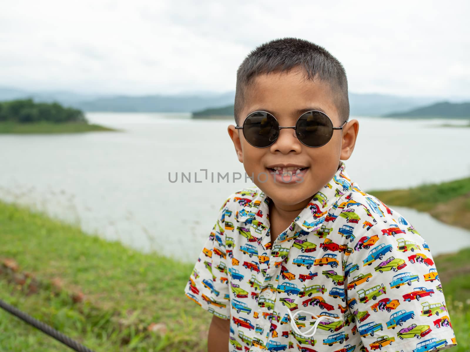 An Asian boy sitting and wearing glasses On the background of the reservoir at the tourist attractions in Thailand.