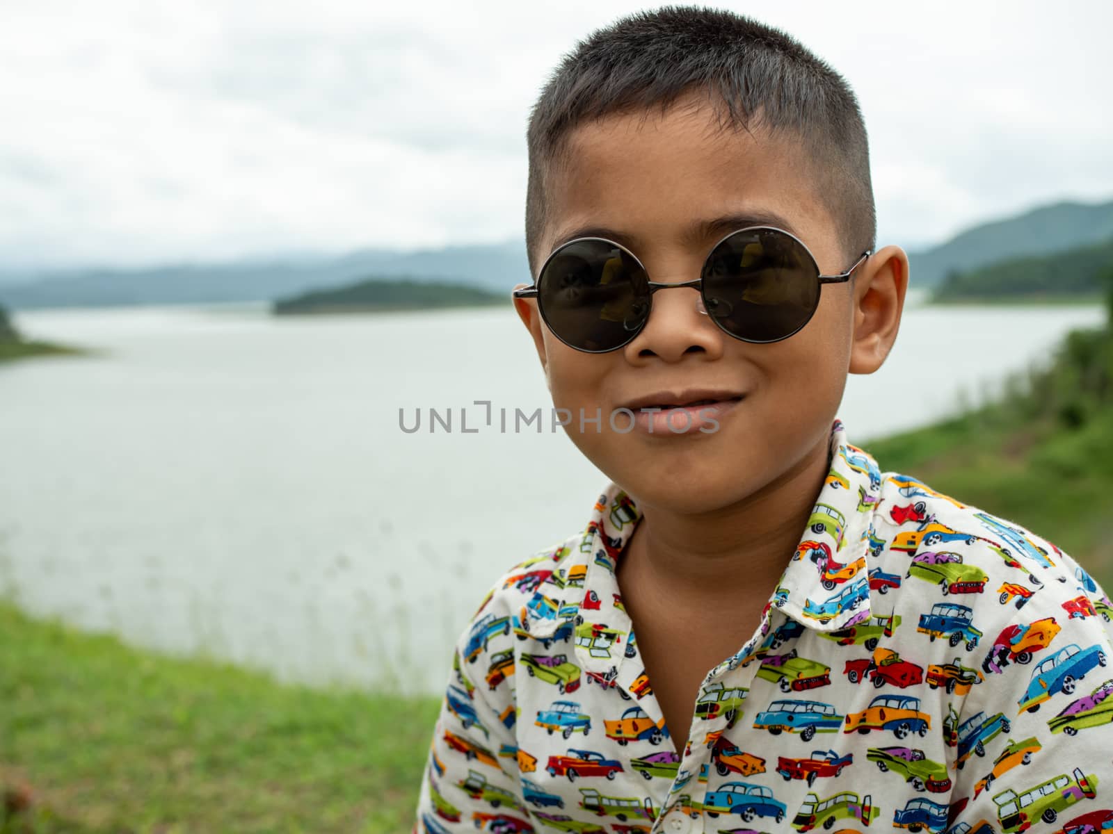 An Asian boy sitting and wearing glasses On the background of the reservoir at the tourist attractions in Thailand.