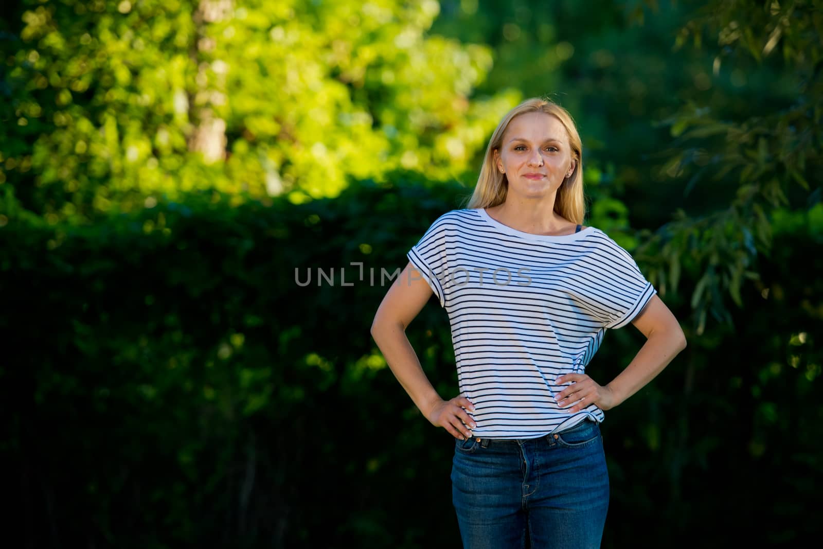 Young woman in jeans and a striped T-shirt posing in the garden. by leonik