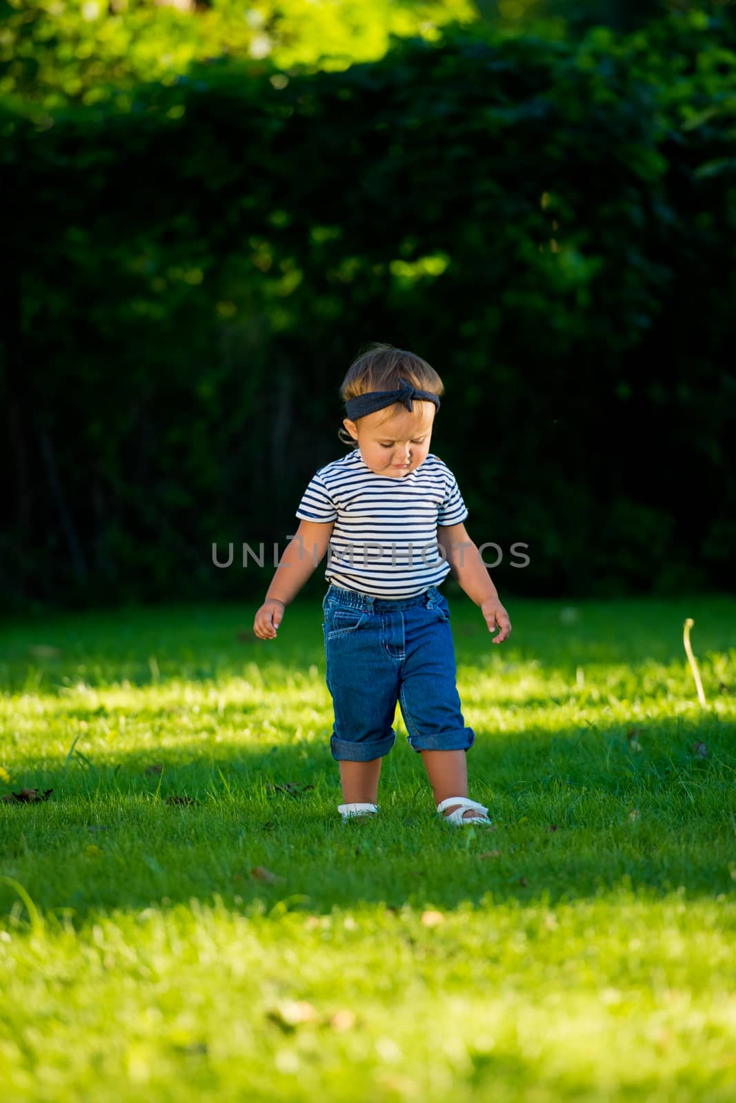 Angry baby girl walking on the lawn in the park.