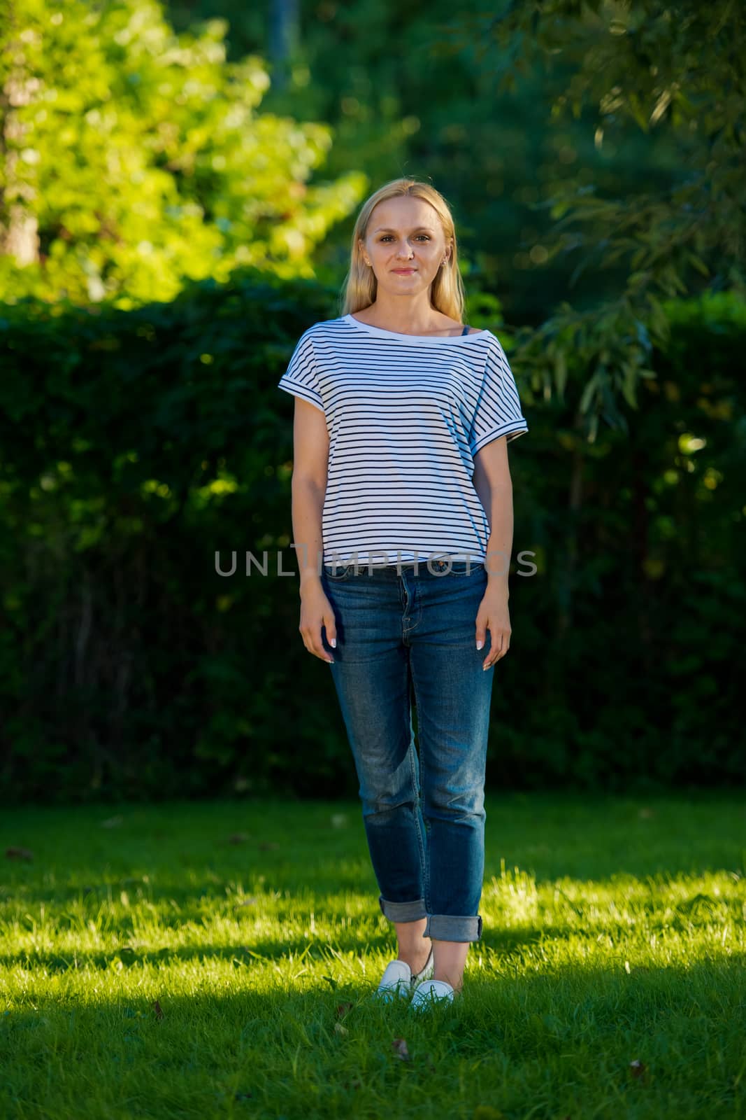 Young woman in jeans and a striped T-shirt posing in the garden.