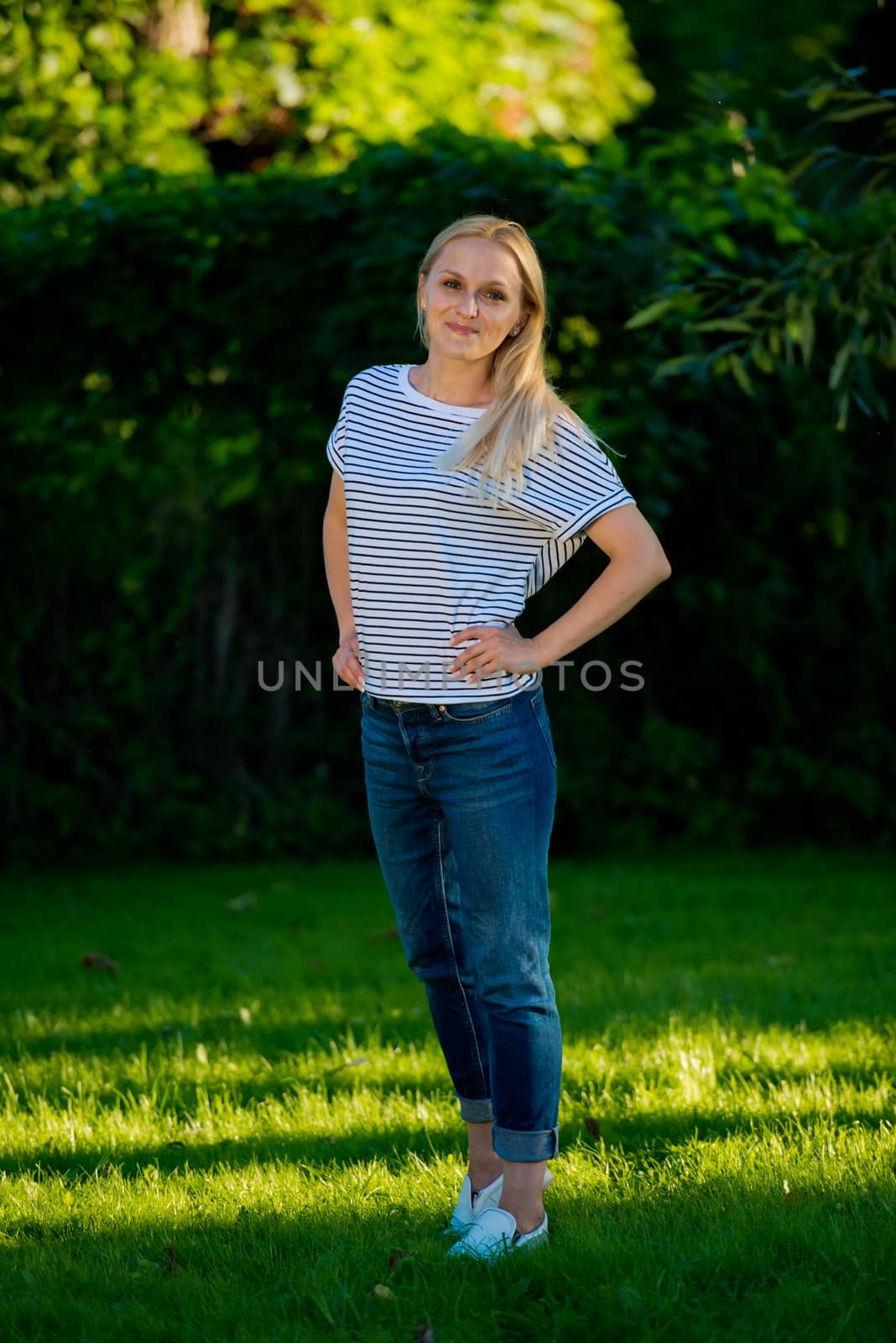 Young woman in jeans and a striped T-shirt posing in the garden. by leonik