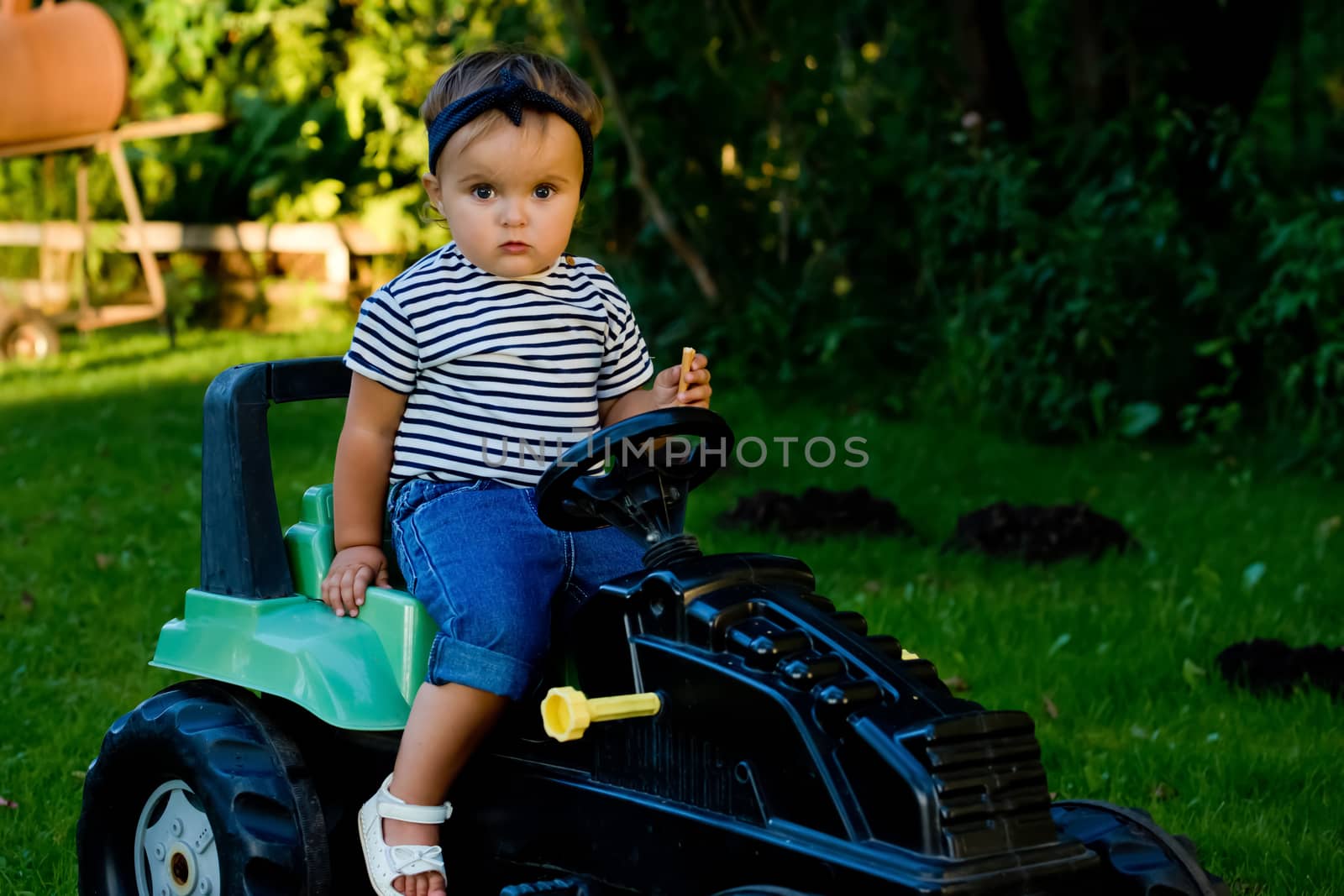 Baby girl playing with toy tractor in a garden. Closeup.