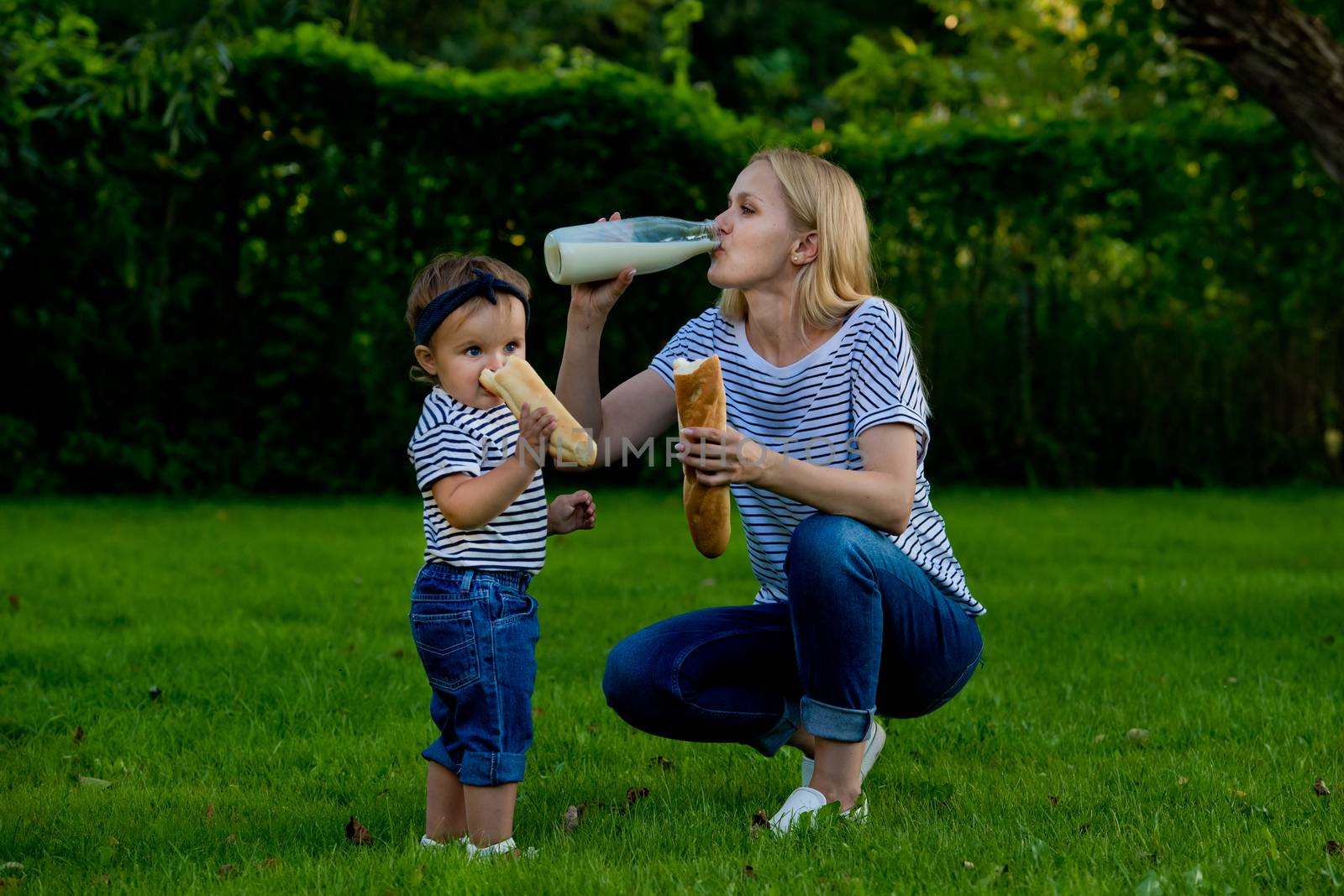 A young woman in jeans and a striped T-shirt drink milk from a glass bottle. Family picnic.
