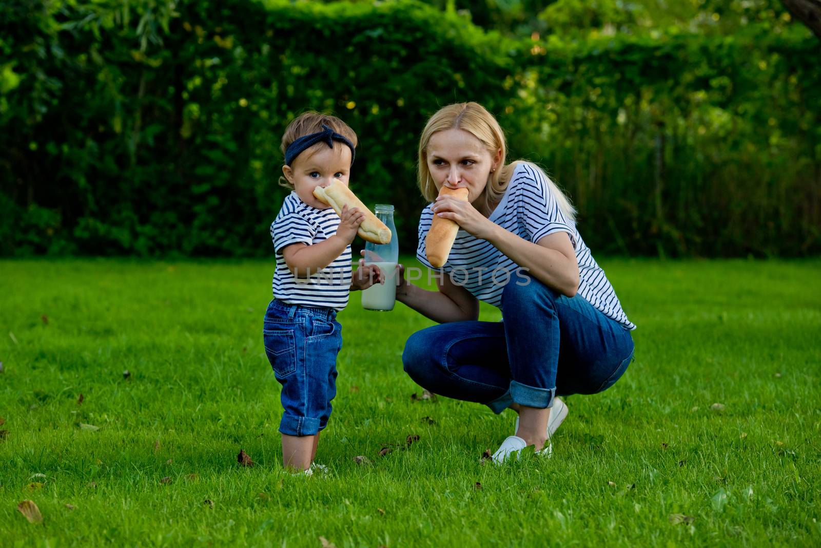 A young woman in jeans and a striped T-shirt and her daughter eating fresh baguett. Family picnic.