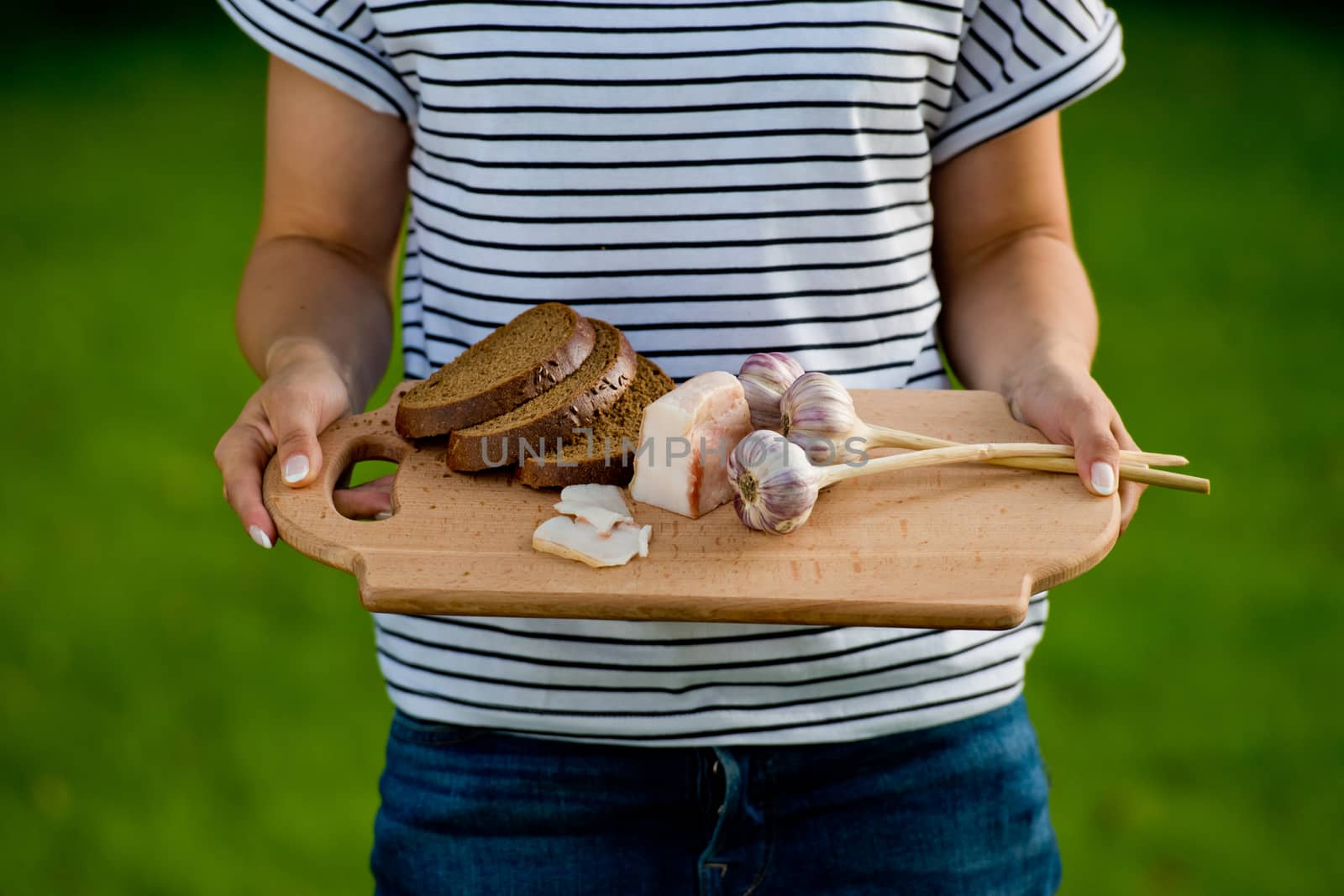 Young woman holding wooden board with garlic, lard and bread. Closeup.