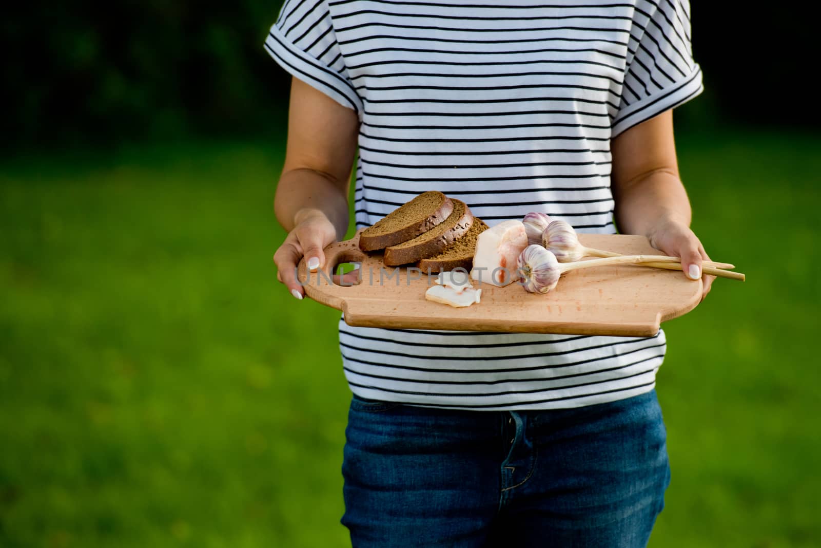 Young woman holding wooden board with garlic, lard and bread. Closeup.