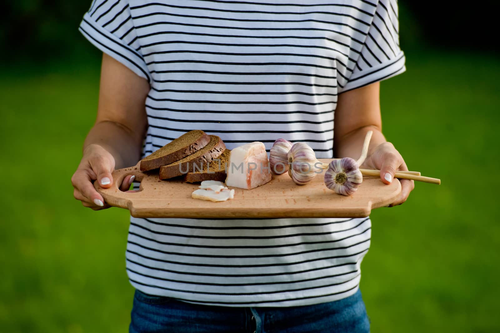 Young woman holding wooden board with garlic, lard and bread. Closeup.