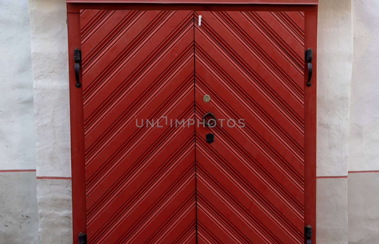 Large red wooden gate with black forged handles and hinges in an old building.
