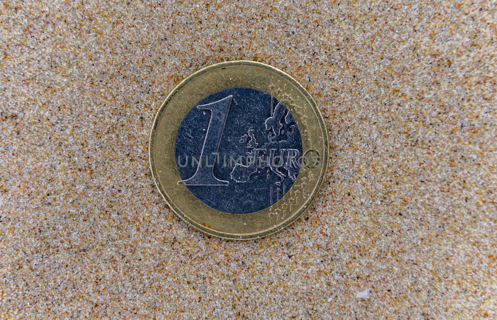 1 euro coin on the wet fine sand of a sea beach.