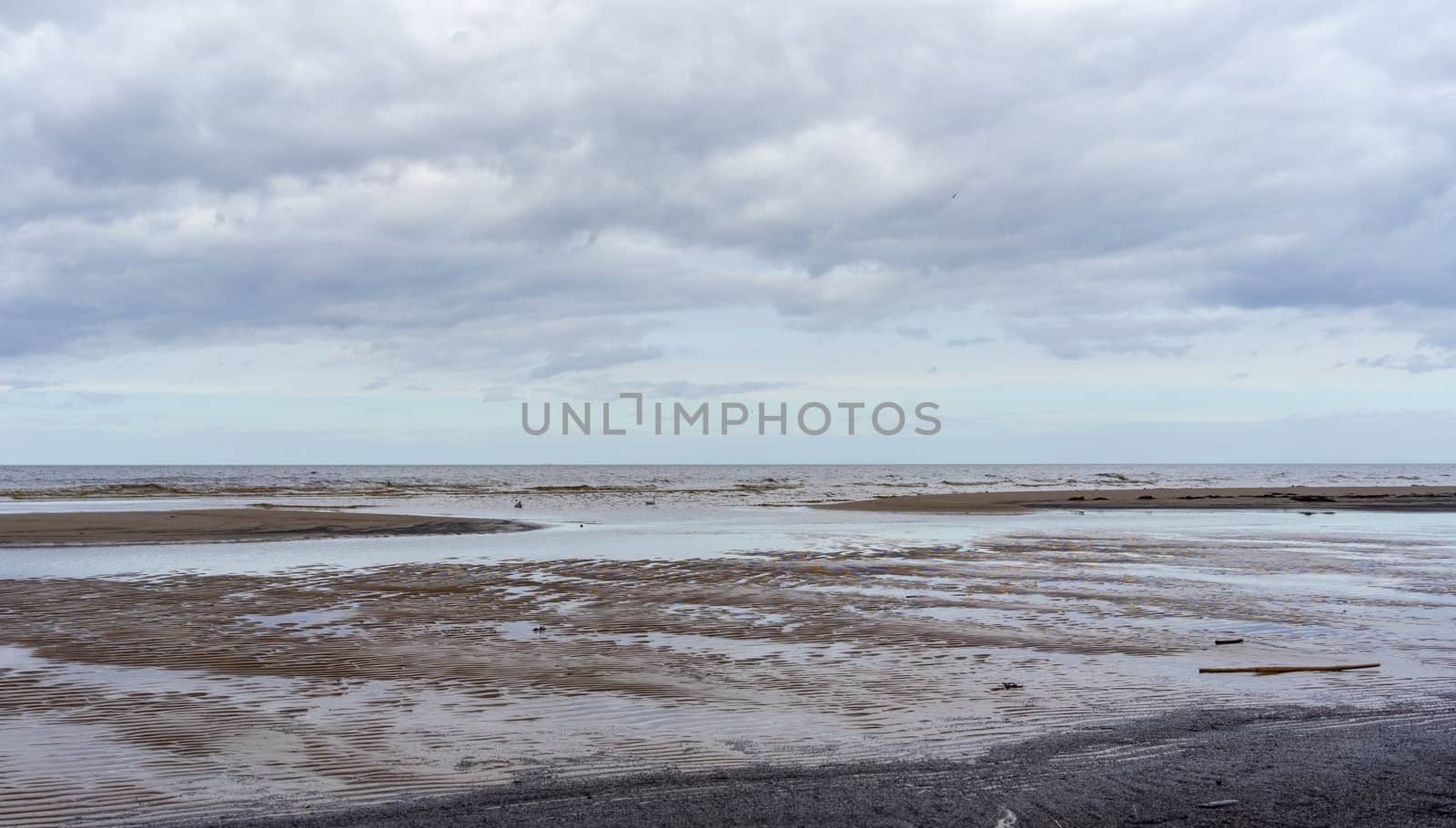 Reflection of clouds in a small lehman on the sandy shore of the Baltic Sea in Jurmala in cloudy weather.