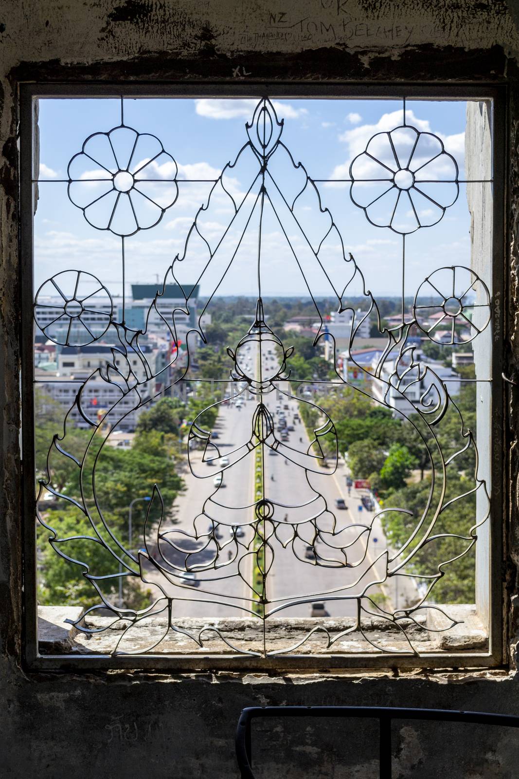 Iron Budha artwork in a window frame, with aerial view of the city streets of Vientiane by kb79