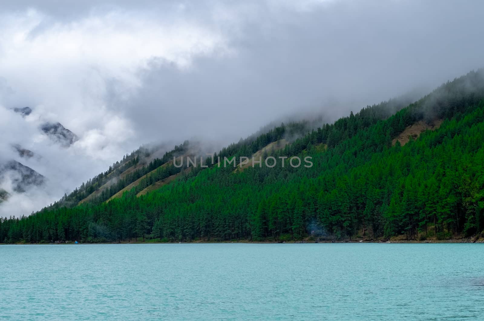 Shavlinskoye lake in the Altai Republic on the background of mountain peaks shrouded in fog.