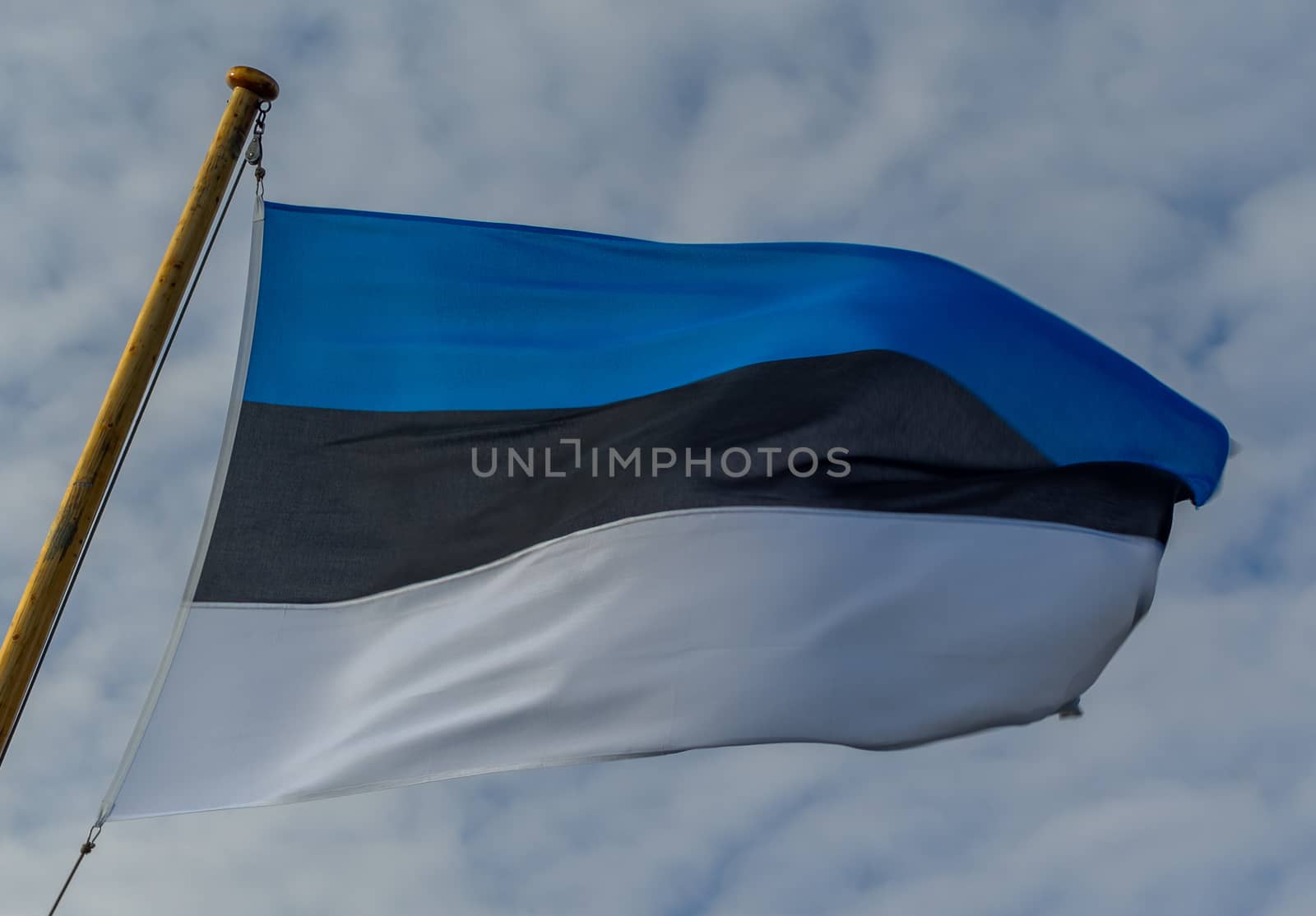 The developing white-black-blue flag of Estonia against the background of clouds in the sky.