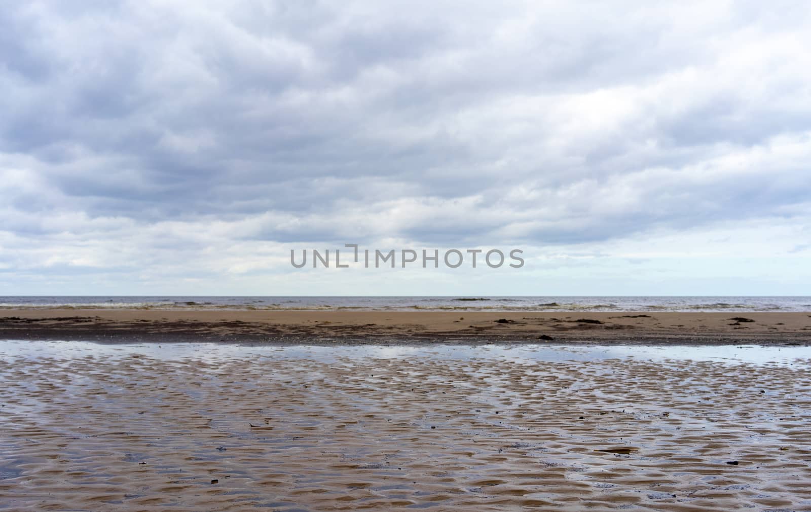 Reflection of clouds in a small lehman on the sandy shore of the Baltic Sea in Jurmala in cloudy weather.